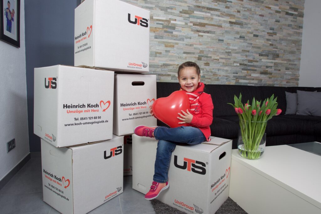 Kind sitzt auf Umzugskartons mit KOCH Logo – Kleines Mädchen auf Umzugskisten, Deutschland