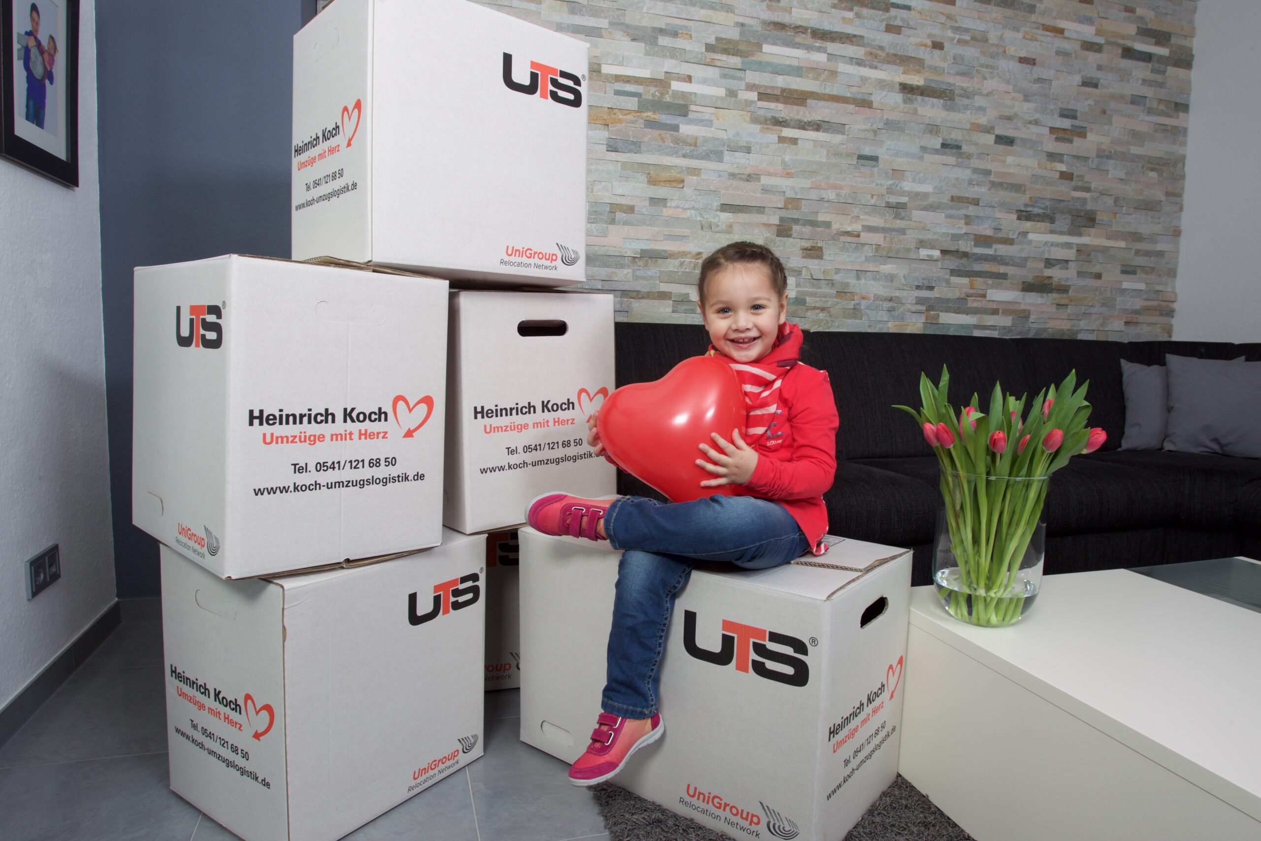 Kind sitzt auf Umzugskartons mit KOCH Logo – Kleines Mädchen auf Umzugskisten, Deutschland