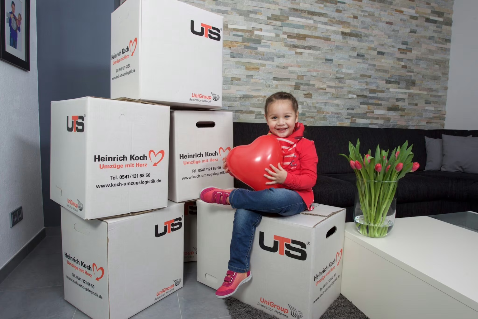 Kind sitzt auf Umzugskartons mit KOCH Logo – Kleines Mädchen auf Umzugskisten, Deutschland