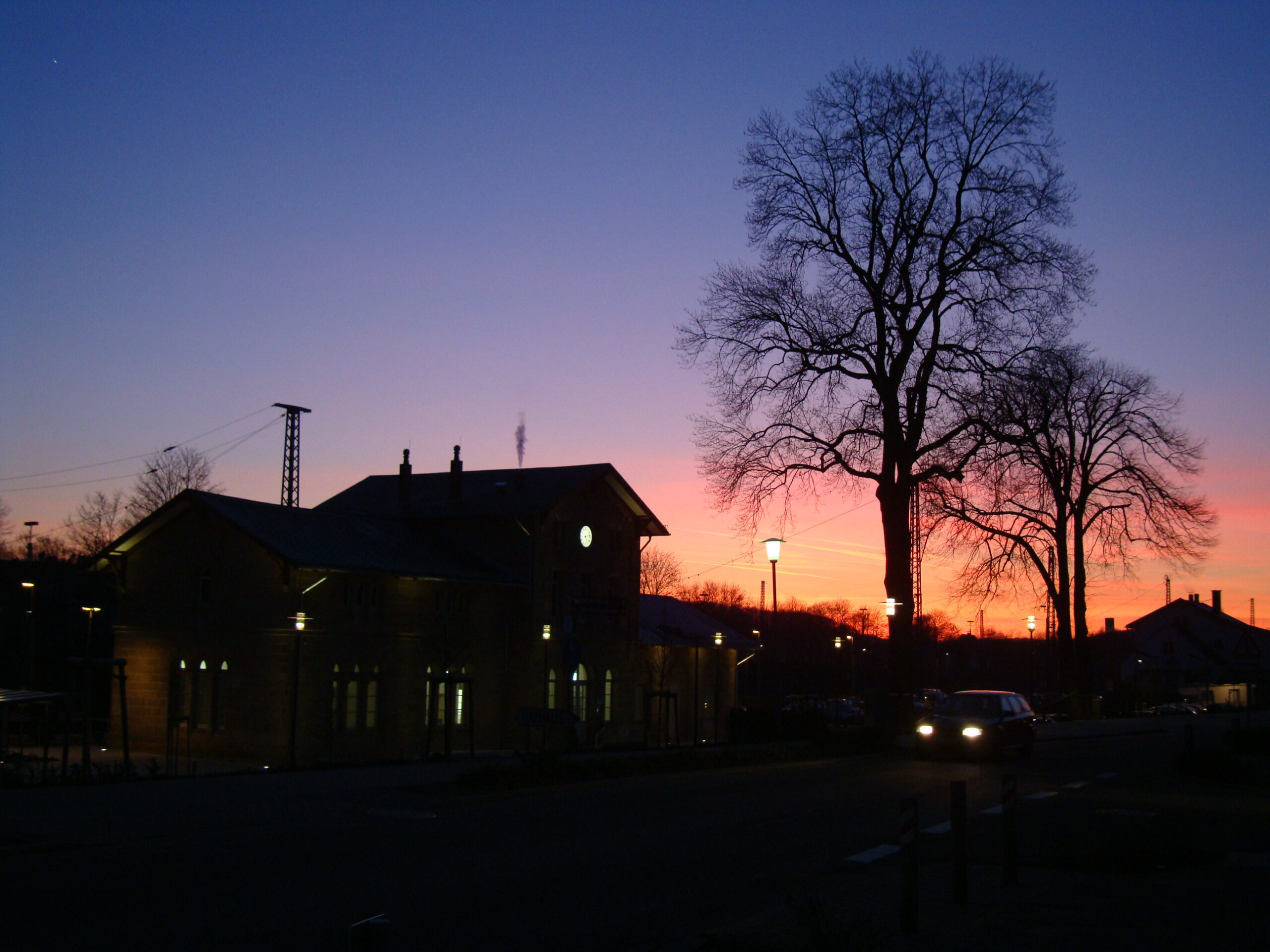 Abendliche Straßenszene mit Bahnhof und Bäumen in Hasbergen.
