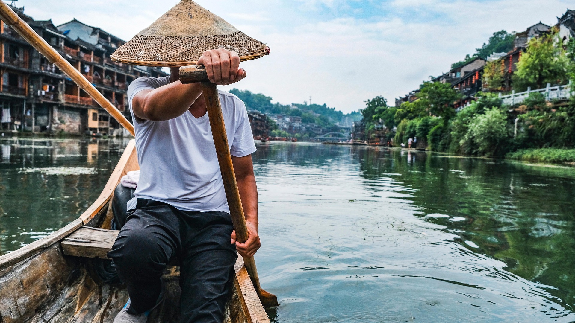 Mann auf Ruderboot mit Altstadt im Hintergrund, China
