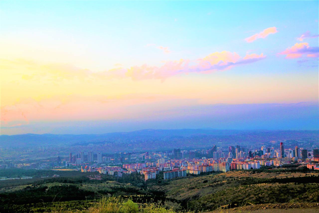 Panoramablick über Ankara, Türkei, bei Sonnenuntergang mit moderner Skyline, Wohnvierteln und sanften Hügeln unter farbenfrohem Abendhimmel.