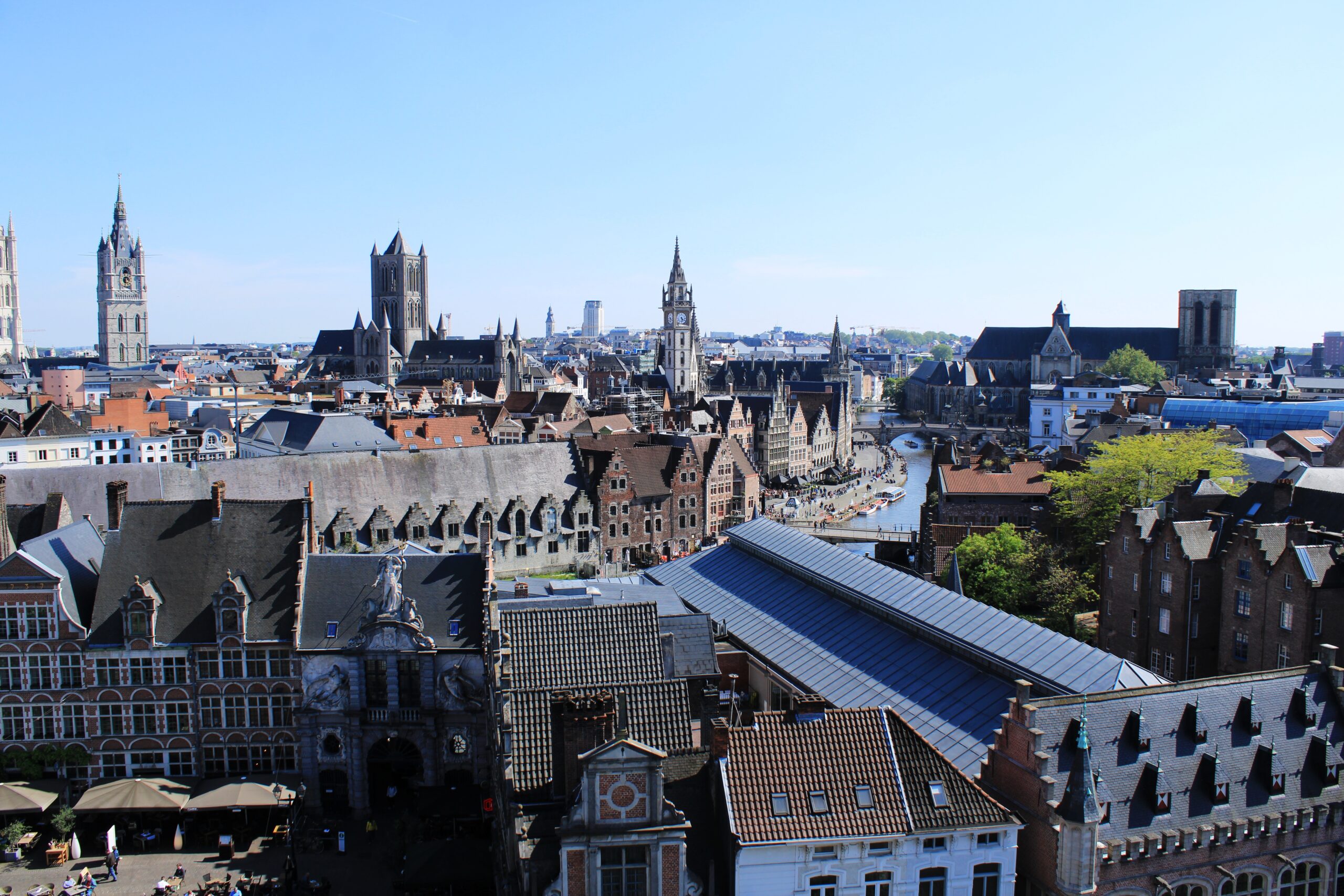 Panoramablick über die historische Altstadt von Gent in Belgien mit mittelalterlichen Gebäuden, Kirchtürmen und Kanälen unter klarem blauem Himmel.