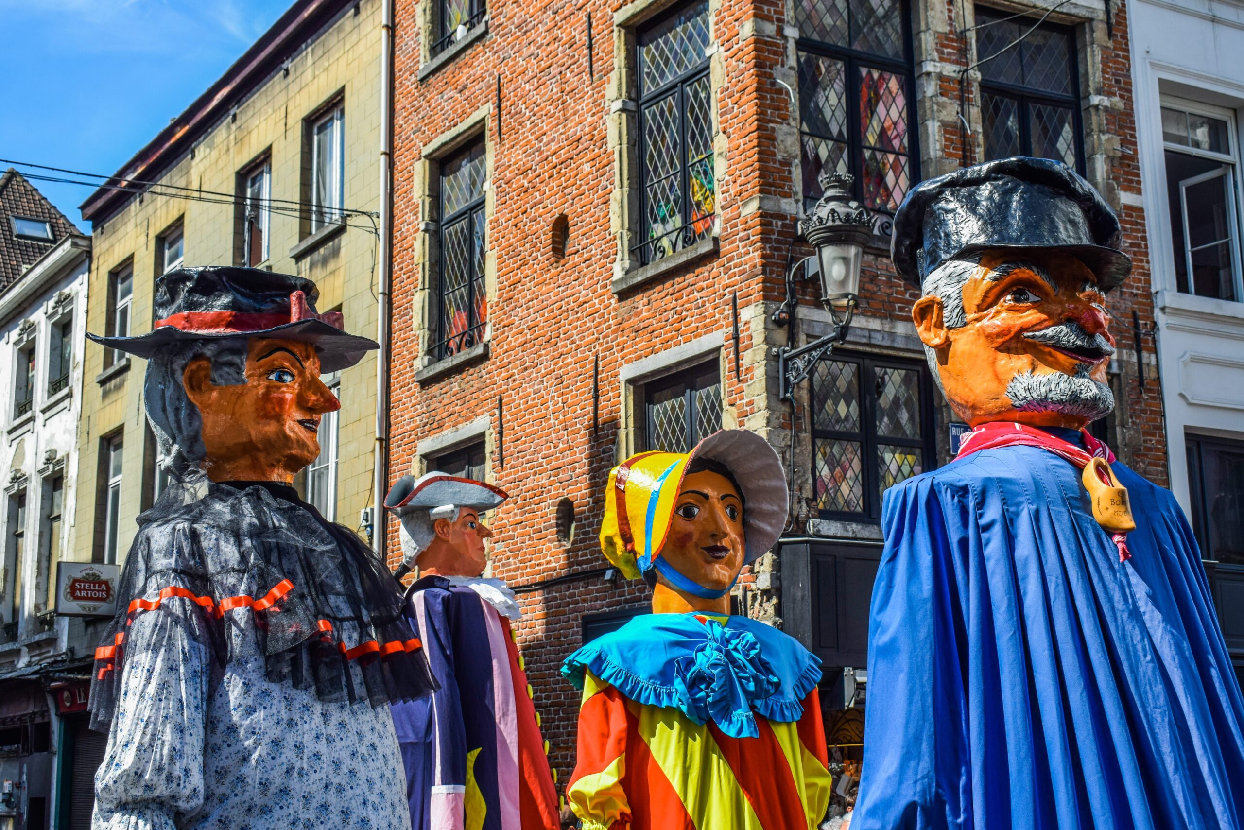 Traditionelle Riesenfiguren bei einem Straßenfest in Belgien vor historischen Backsteingebäuden mit bunten Kostümen und kultureller Folklore.