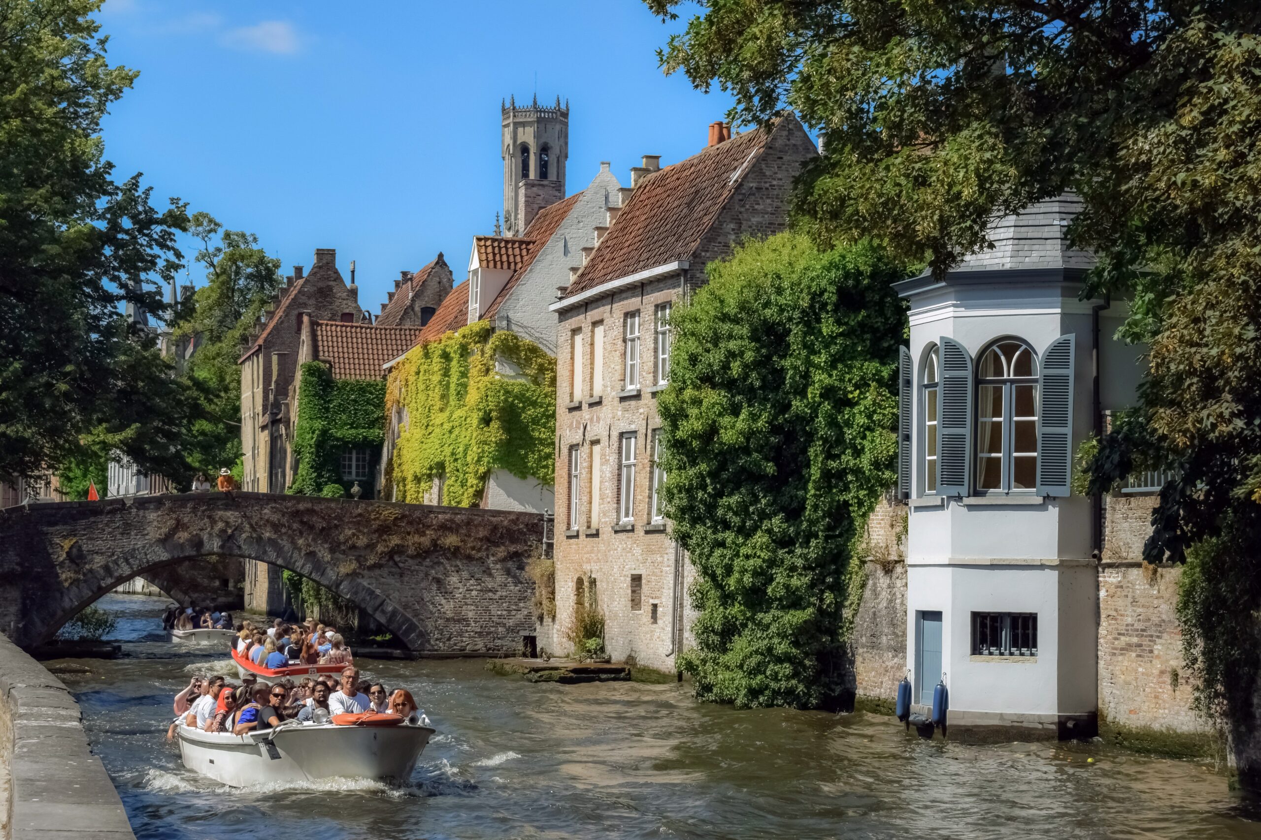 Brügge – Kanal mit efeubewachsenen alten Häusern und Menschen auf Booten, Belgien
