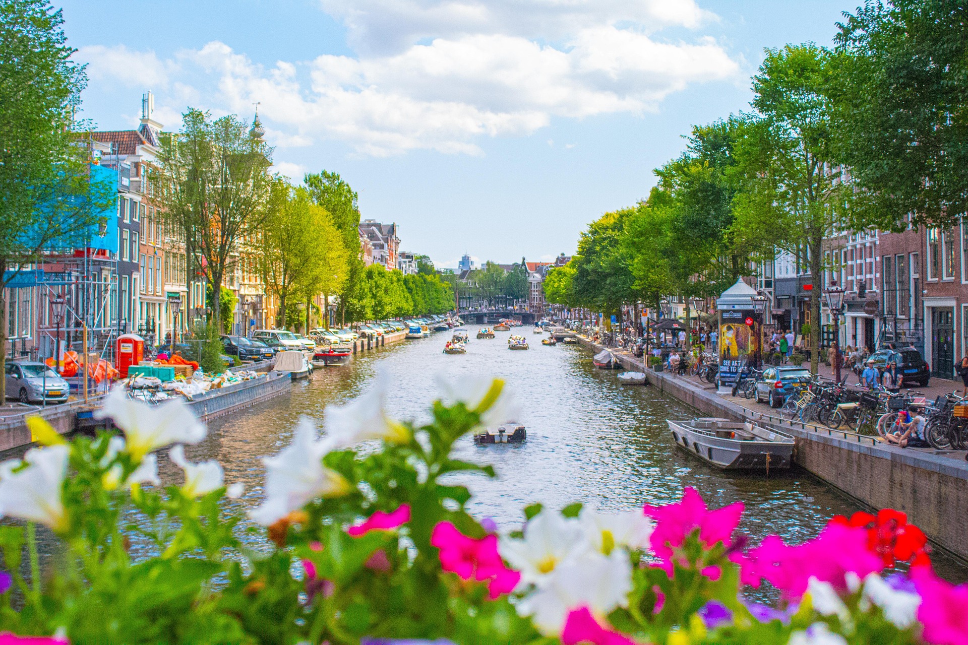 Amsterdam – Kanal mit Booten, Blumen und grünen Bäumen, Niederlande