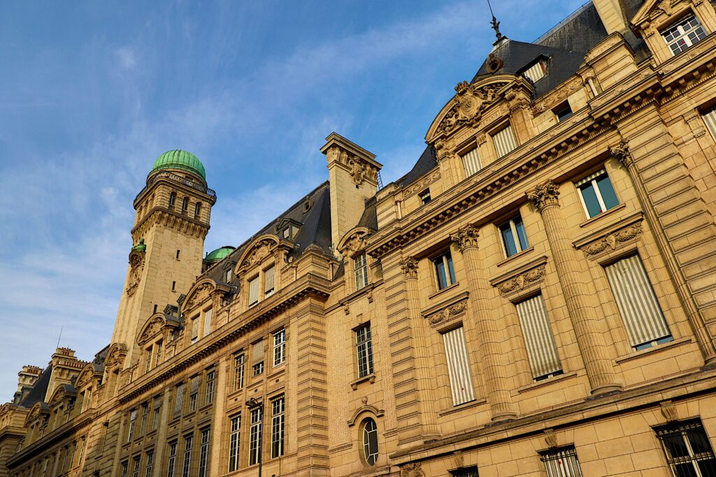 Historisches Gebäude mit klassischer Beaux-Arts-Architektur und grünem Kuppelturm in Frankreich unter blauem Himmel mit kunstvoller Steinfassade.