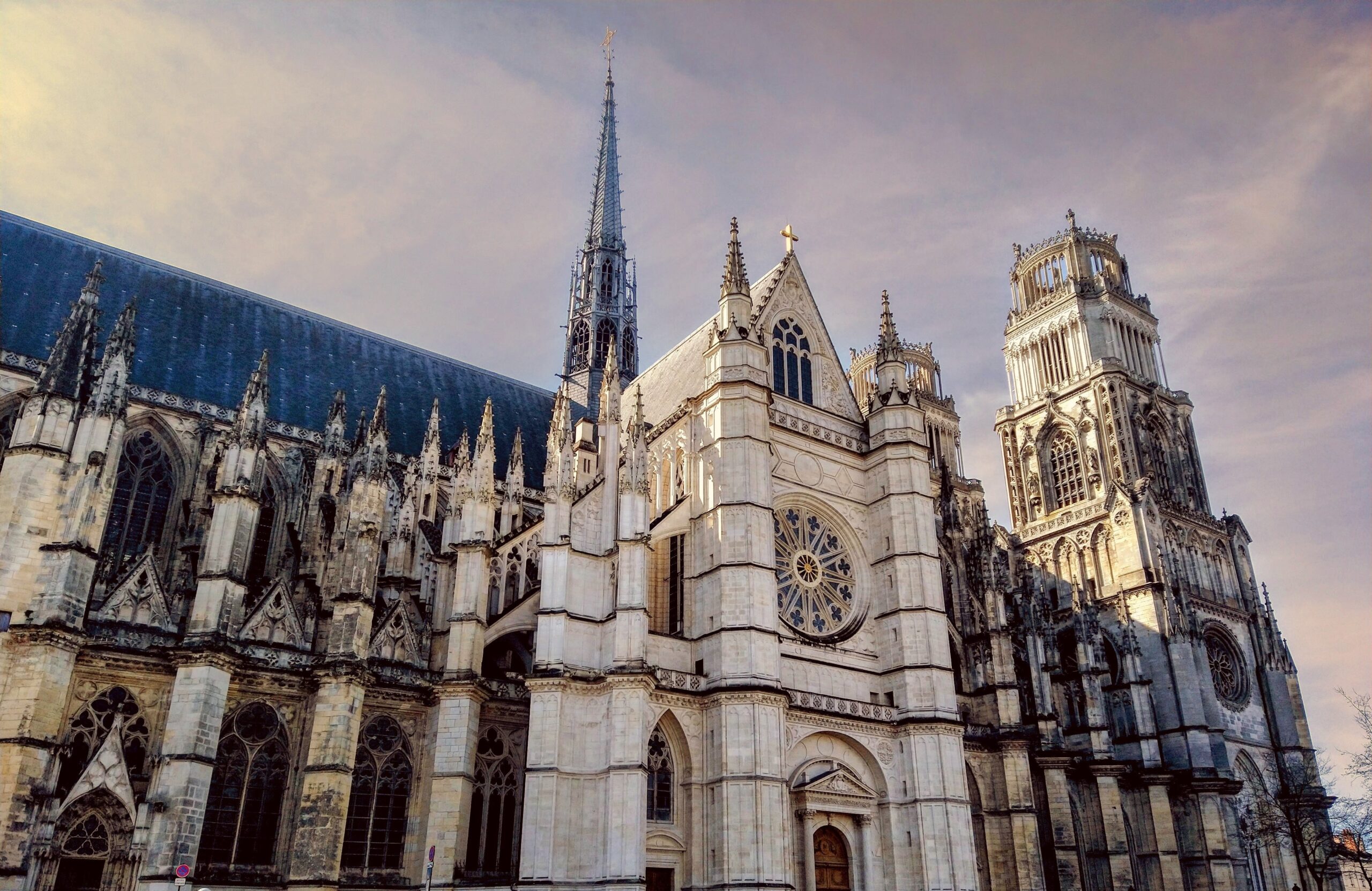 Gotische Kathedrale in Frankreich mit kunstvollen Türmen, Rosettenfenstern und imposanter mittelalterlicher Architektur bei stimmungsvollem Abendhimmel.