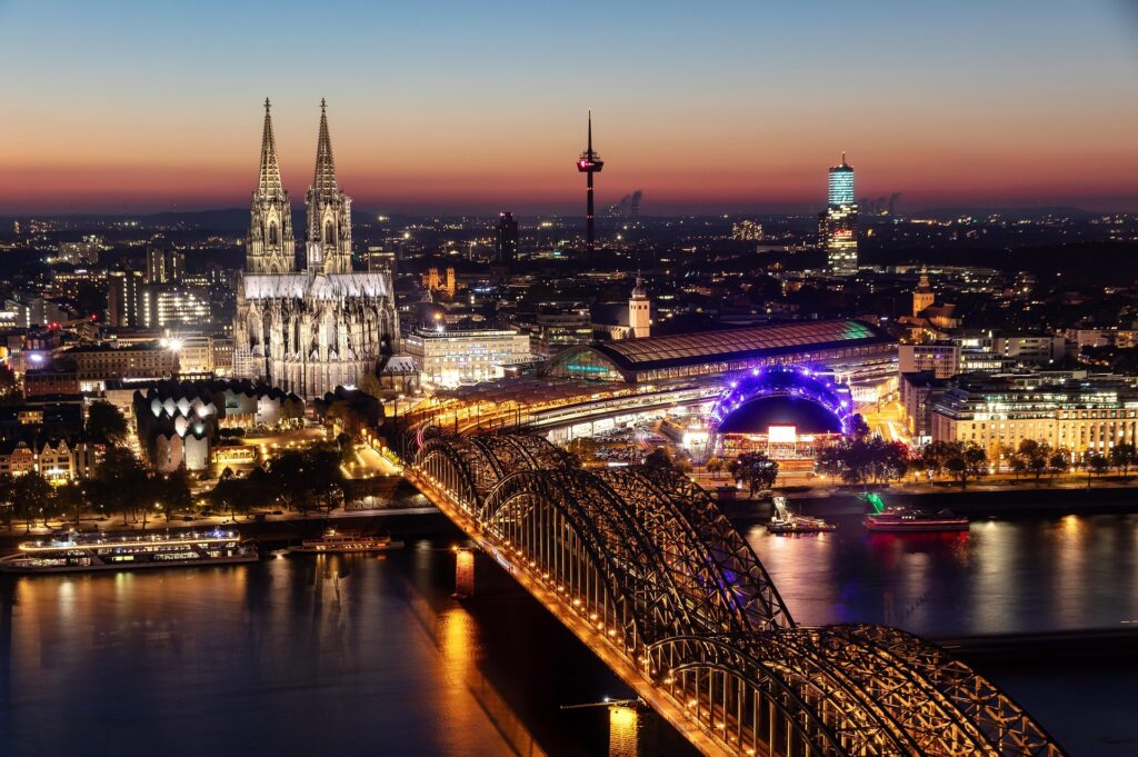 Köln – Nächtliche Vogelperspektive auf den beleuchteten Kölner Dom, die Hohenzollernbrücke und die Altstadt am Rhein, Nordrhein-Westfalen, Deutschland